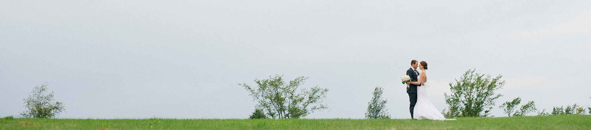 Portrait in the country outside of Ottawa of bride and groom on their wedding day in a wide field under dark dramatic skies.